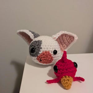 May include: A white and gray crocheted plush toy with pink ears and a red crocheted bird plush toy with black eyes.