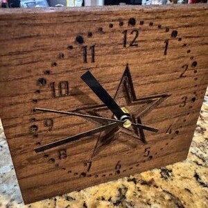 Könnte beinhalten: Eine Holzuhr mit einem Sternmuster und schwarzen Zeigern. Das Zifferblatt der Uhr hat römische Ziffern und ist von einem Punktkreis umgeben.