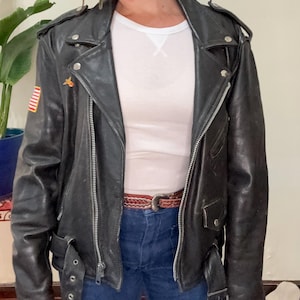 May include: A black leather motorcycle jacket with a zipper closure, a belt at the waist, and a small American flag patch on the left sleeve.