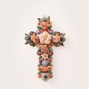 Puede incluir: Una cruz decorativa adornada con flores y mariposas coloridas. La cruz presenta una gran flor central de color melocotón, rodeada de flores más pequeñas en tonos naranja, azul y verde. El diseño incluye detalles de mariposas.