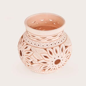 May include: A light peach-colored ceramic vase with intricate cut-out floral and leaf designs. The vase has a wide opening and a decorative band near the top. The detailed carvings create a textured surface, perfect for home decor.