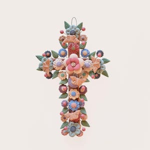 May include: A decorative wall cross crafted from clay, featuring a central arrangement of sculpted flowers and butterflies in muted pastel tones of pink, blue, and green. The cross is adorned with small spherical accents and green leaves.