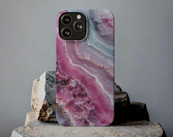 May include: A smartphone case with a pink, white, and gray agate stone pattern. The case has a glossy finish and a camera cutout. The case is displayed on a rough stone surface against a gray background.