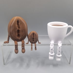 Könnte beinhalten: Drei 3D-gedruckte Figuren: zwei braune Kaffeebohnen mit Beinen und eine weiße Kaffeetasse mit Beinen. Die Figuren sitzen auf einem durchsichtigen Acrylregal.