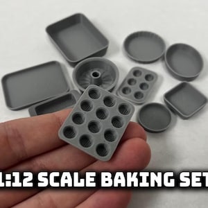 May include: A collection of gray miniature baking pans, including rectangular, round, and muffin tins. The set is held in a hand and labeled "1:12 SCALE BAKING SET". These small baking tools are perfect for dollhouses or miniature projects.