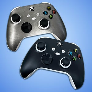 May include: Two Xbox controllers, one in brushed silver and the other in matte black, are displayed against a gradient blue background. Both controllers have white accents, black joysticks, and colored action buttons (green, red, blue, yellow).