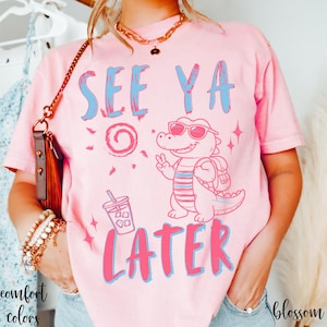 May include: Pink t-shirt with the text "SEE YA LATER" in blue and pink. A cartoon alligator wearing sunglasses and a backpack is giving a peace sign. A drink with ice and a straw is also shown.