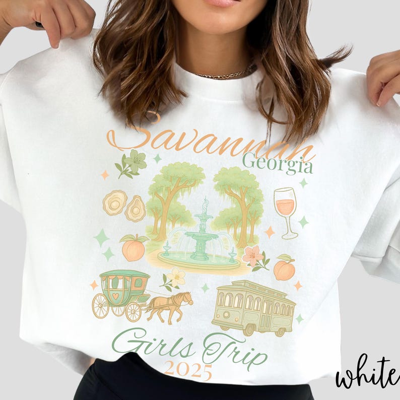 May include: White sweatshirt with a colorful graphic design featuring the text "Savannah Georgia Girls Trip 2025." The design includes illustrations of a fountain, trees, a horse-drawn carriage, a trolley, and peaches.