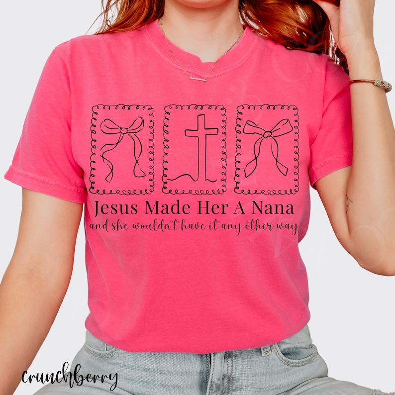 Pu&ograve; includere: Una maglietta rosa acceso con la scritta "Jesus Made Her A Nana and she wouldn't have it any other way." Il design include una croce e due illustrazioni di fiocchi neri. La maglietta &egrave; a girocollo.