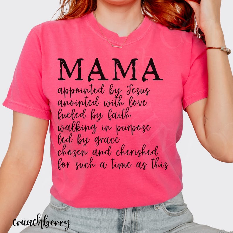 May include: A pink t-shirt with the word "MAMA" in large black letters. Below the word are several lines of text that read "appointed by Jesus, anointed with love, fueled by faith, walking in purpose, led by grace, chosen and cherished for such a time as this."