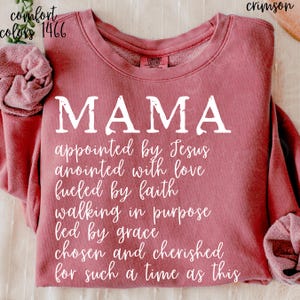 May include: Crimson-colored sweatshirt with the word "MAMA" in large white letters. Below, a list of inspirational phrases is printed in white. The sweatshirt has the Comfort Colors brand label.