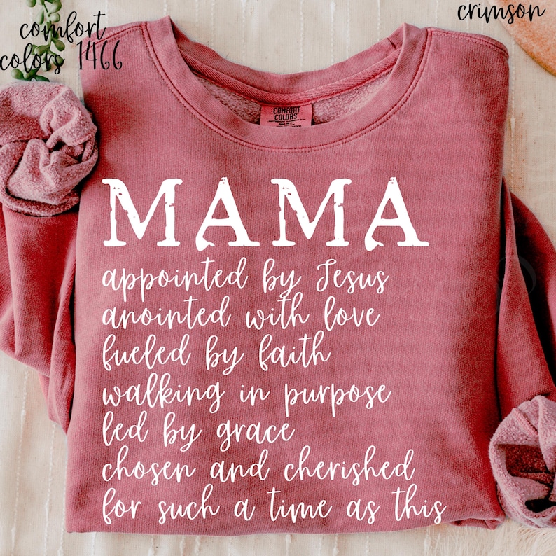 May include: Crimson-colored sweatshirt with the word "MAMA" in large white letters. Below, a list of inspirational phrases is printed in white. The sweatshirt has the Comfort Colors brand label.