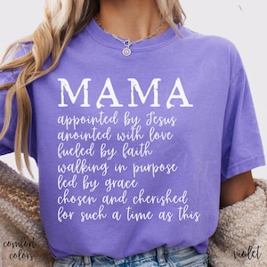 May include: A violet-colored t-shirt with the word "MAMA" in large white letters. Below, smaller white text reads "appointed by Jesus, anointed with love, fueled by faith, walking in purpose, led by grace, chosen and cherished for such a time as this."