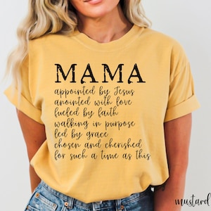 May include: Mustard-colored t-shirt with the word "MAMA" in large black letters. Below the word "MAMA" is a list of inspirational phrases. The shirt is made of a soft material and is a comfortable fit.