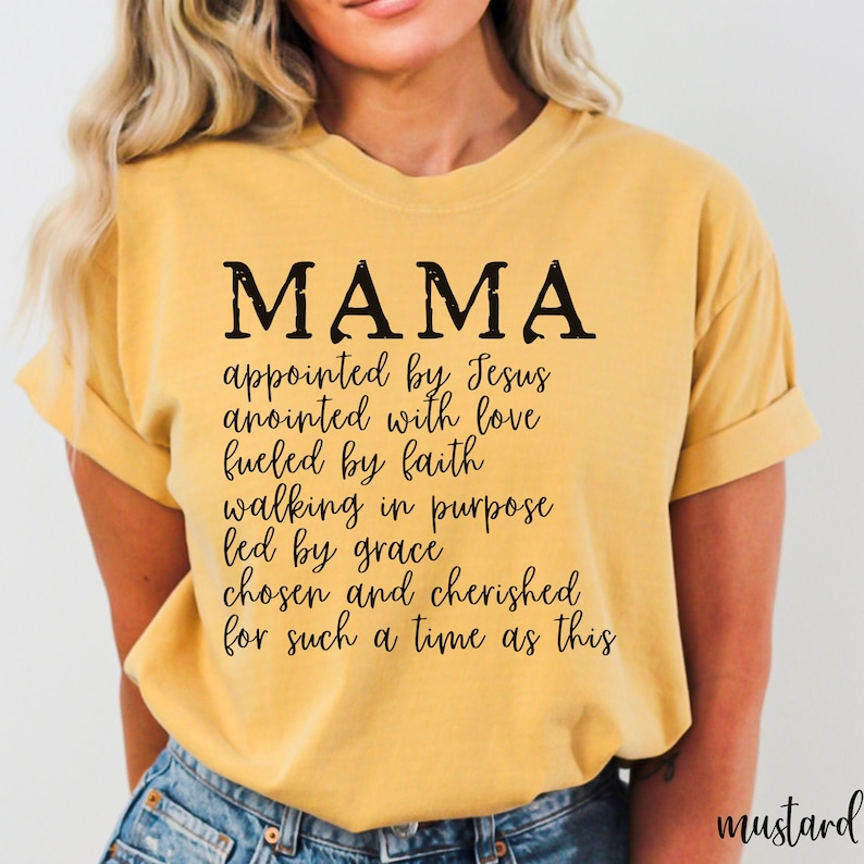 May include: Mustard-colored t-shirt with the word "MAMA" in large black letters. Below the word "MAMA" is a list of inspirational phrases. The shirt is made of a soft material and is a comfortable fit.