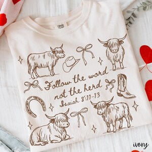 May include: Ivory-colored sweatshirt with a brown graphic design featuring Highland cows, a cowboy hat, a horseshoe, a cowboy boot, and bows. The text "Follow the word not the herd Isaiah 8:11-13" is also printed on the shirt.