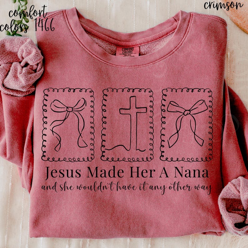 Pu&ograve; includere: Felpa color cremisi con la scritta "Jesus Made Her A Nana and she wouldn't have it any other way." Il design include tre immagini incorniciate: due fiocchi e una croce. La felpa &egrave; una Comfort Colors 1466.