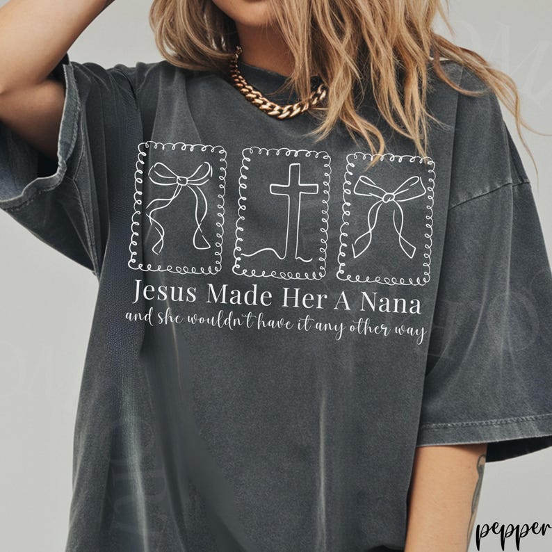 Pu&ograve; includere: T-shirt grigio scuro con la scritta "Jesus Made Her A Nana and she wouldn't have it any other way." La maglietta presenta tre disegni bianchi incorniciati: due fiocchi e una croce.