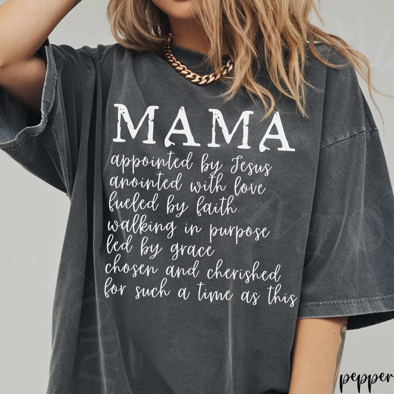 May include: Dark gray t-shirt with the word "MAMA" in large white letters. Below, a list of inspirational phrases is printed in white. The shirt has a relaxed fit and a vintage look.