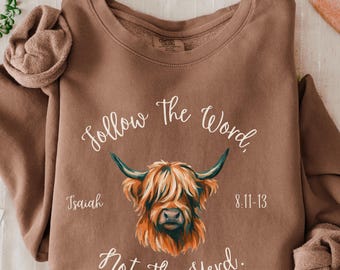 May include: Espresso-colored sweatshirt with the text "Follow The Word, Not The Herd" and a Highland cow illustration. The text "Isaiah 8:11-13" is also included. The sweatshirt is a Comfort Colors 1466 style.