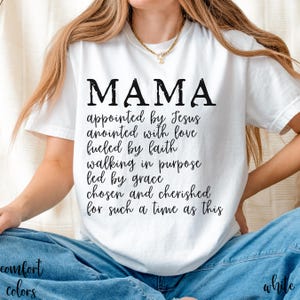 May include: White t-shirt with the word "MAMA" in large black letters. Below the word "MAMA" is a list of inspirational phrases. The shirt is part of the "Comfort Colors" collection.