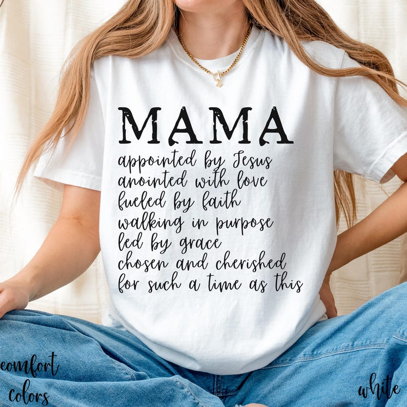May include: White t-shirt with the word "MAMA" in large black letters. Below the word "MAMA" is a list of inspirational phrases. The shirt is part of the "Comfort Colors" collection.