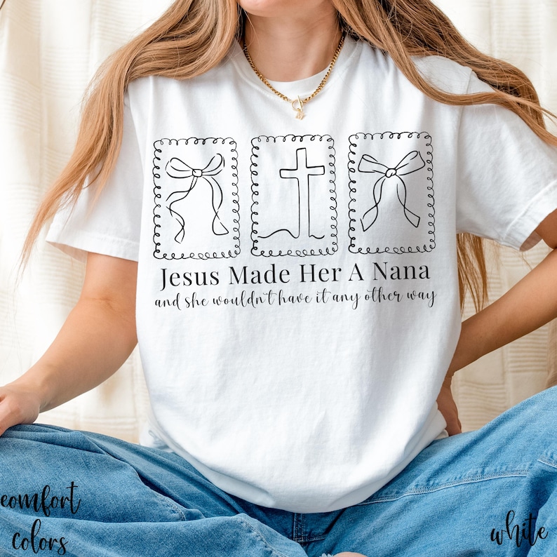 Pu&ograve; includere: T-shirt bianco con un design grafico nero raffigurante una croce e due fiocchi all'interno di cornici decorative. Il testo "Jesus Made Her A Nana and she wouldn't have it any other way" &egrave; stampato sotto. La maglietta &egrave; abbinata a jeans blu.
