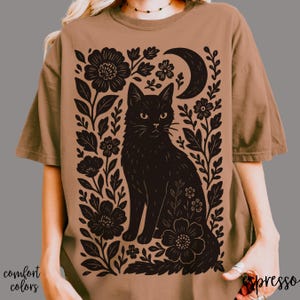 May include: Espresso-colored t-shirt featuring a black cat illustration surrounded by floral and crescent moon designs. The words "comfort colors" are printed on the bottom left. The word "espresso" is printed on the bottom right.