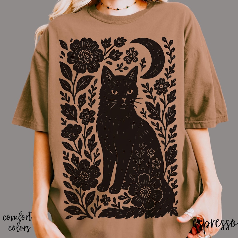 May include: Espresso-colored t-shirt featuring a black cat illustration surrounded by floral and crescent moon designs. The words "comfort colors" are printed on the bottom left. The word "espresso" is printed on the bottom right.