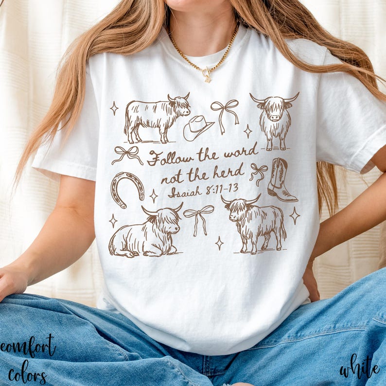 May include: White t-shirt with a brown graphic design featuring Highland cows, a cowboy hat, boots, and bows. The text "Follow the word not the herd Isaiah 8:11-13" is also printed on the shirt.