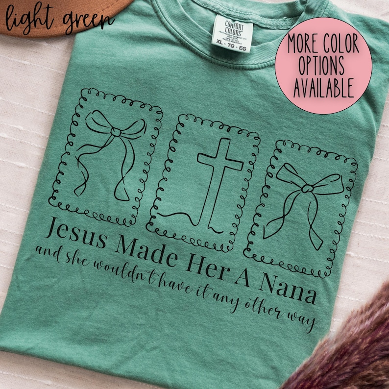 Pu&ograve; includere: T-shirt verde chiaro con la scritta "Jesus Made Her A Nana and she wouldn't have it any other way." Il design include tre illustrazioni incorniciate: due fiocchi e una croce. La maglietta ha un girocollo e un'etichetta "Comfort Colors".