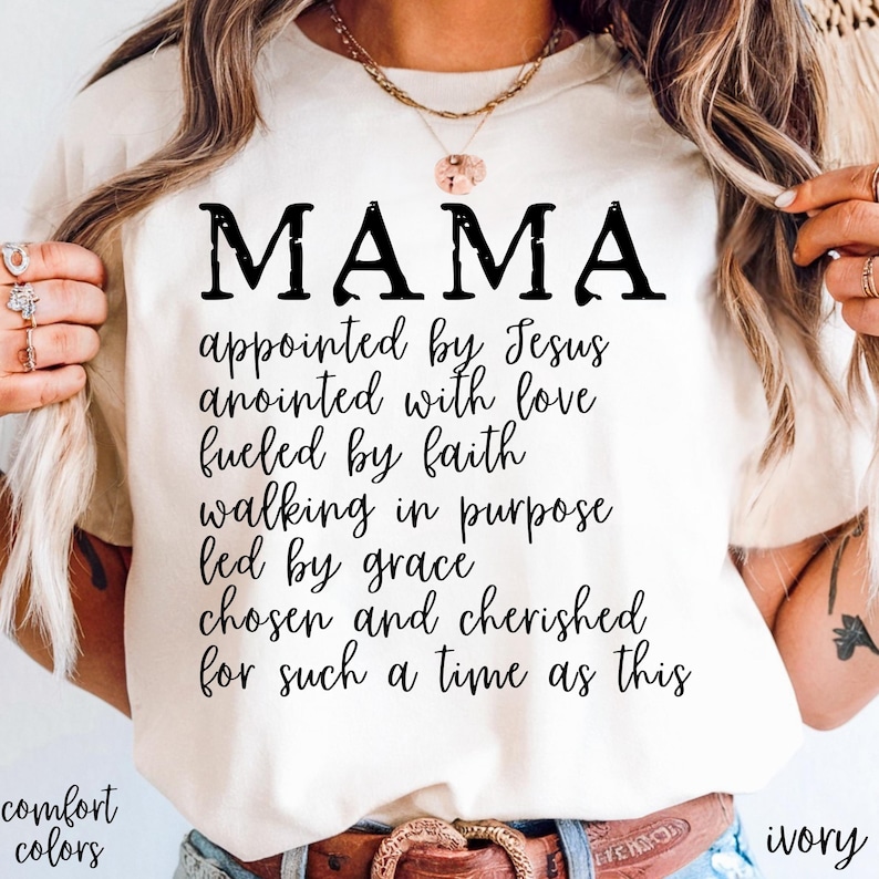 May include: Ivory-colored t-shirt with the word "MAMA" in large, black letters. Below, a list of inspirational phrases is printed in a script font. The words "comfort colors" and "ivory" are also visible.