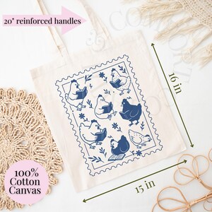 May include: Cream tote bag with a blue stamp design of chickens reading books. The bag is 38 cm wide, 41 cm tall, and has 51 cm reinforced handles. Made of 100% cotton canvas.