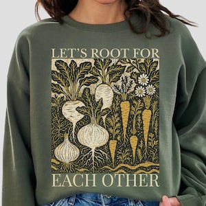 May include: Green sweatshirt with a graphic featuring various root vegetables and the text "LET'S ROOT FOR EACH OTHER" in a rectangular design. The vegetables are in shades of white, gold, and brown.