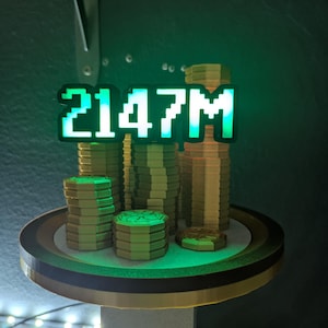 May include: A 3D-printed display featuring stacks of gold-colored coins on a round platform. The display has a green neon sign that reads "2147M". The platform is supported by a gray stand, and the background is dark green.