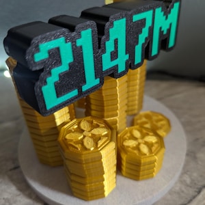 May include: A 3D-printed sculpture featuring stacks of gold-colored coins and the text "2147M" in black and green. The coins have a floral design on top and are arranged on a white circular base.