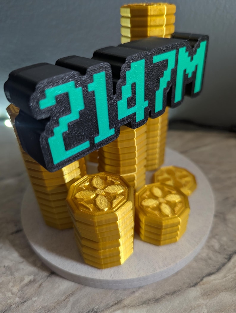 May include: A 3D-printed sculpture featuring stacks of gold-colored coins and the text "2147M" in black and green. The coins have a floral design on top and are arranged on a white circular base.