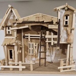 May include: A handcrafted wooden miniature house with a rustic design. The model features a multi-level structure with a ladder, fences, and various architectural details. The house is constructed from small wooden pieces, showcasing a natural wood colour.