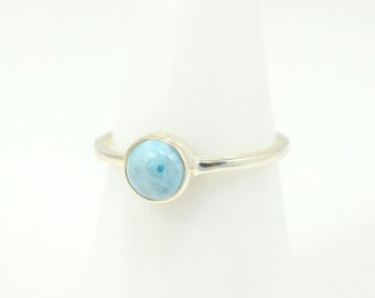 May include: A silver ring with a light blue gemstone. The ring is on a white display stand.