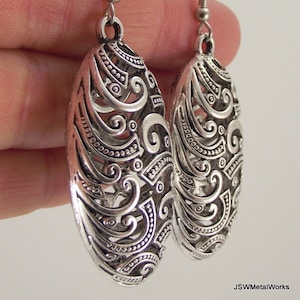 May include: Silver filigree earrings with a swirl design. The earrings are oval shaped and have a hook fastening.