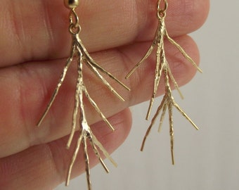 May include: Gold-toned earrings with a delicate, branch-like design. The earrings are made of metal and have a textured finish.