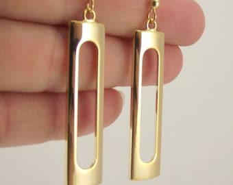 Puede incluir: Pendientes de aro dorados con forma rectangular y un corte en el centro. Los pendientes tienen un diseño simple y moderno.