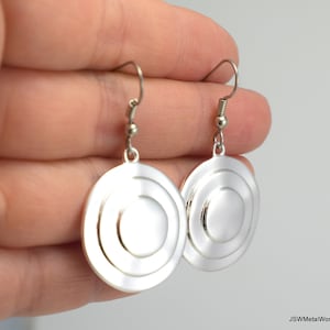 May include: Silver tone earrings with a circular design featuring three concentric circles. The earrings have a simple hook closure.