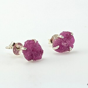May include: A pair of silver earrings with pink rough cut gemstones. The earrings are set in a simple design with a small silver post and a small silver backing.