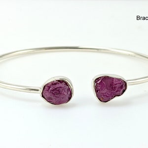 May include: A silver bangle bracelet with two raw ruby stones. The bracelet is open and has a simple design. Bracelet A.