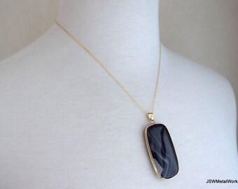 Puede incluir: Un collar de cadena de oro con un colgante de ágata negro y blanco. El colgante es rectangular y tiene un acabado liso y pulido.
