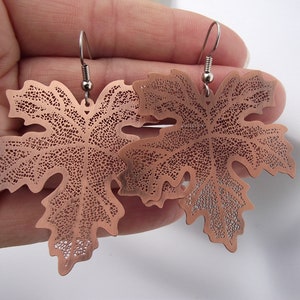 May include: A pair of copper leaf earrings with a delicate, intricate design. The earrings are made of a thin, lightweight metal and have a slightly oxidized finish.