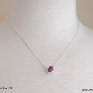 May include: A silver chain necklace with a small, faceted, purple gemstone pendant.