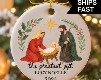 May include: A round Christmas ornament with a religious theme. The ornament features a nativity scene with Mary, Joseph, and baby Jesus. The text "the greatest gift" and "LUCY NOELLE 2025" are also on the ornament.