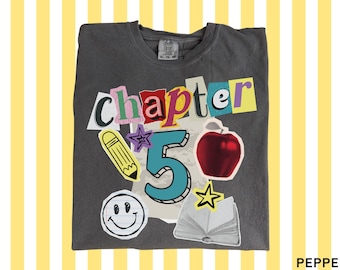 Peut inclure: Un t-shirt gris anthracite avec un motif style collage affichant le texte "chapter 5" en lettres colorées façon lettre anonyme. Le design comprend un crayon jaune, une pomme rouge, un visage souriant, une étoile et un livre ouvert.